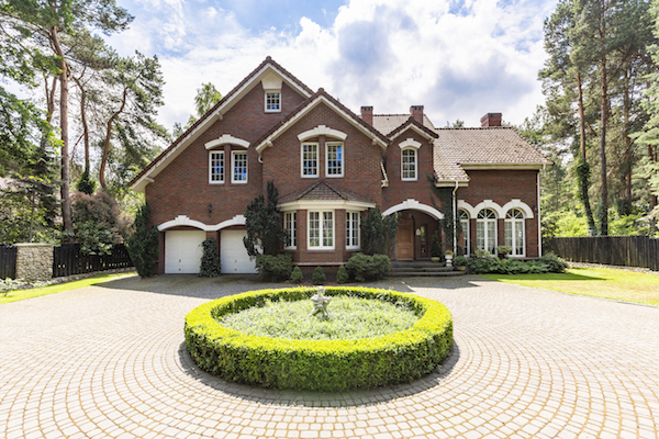 Front view of a driveway with a round garden and big, english style house in the background. Real photo